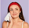 Woman cleaning her face with a towel against a purple background