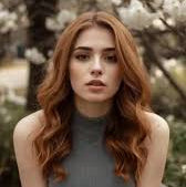 Woman with long brown hair sitting outdoors with cherry blossom trees in the background