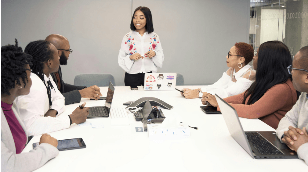 Business meeting with diverse professionals collaborating around a conference table with laptops and devices.