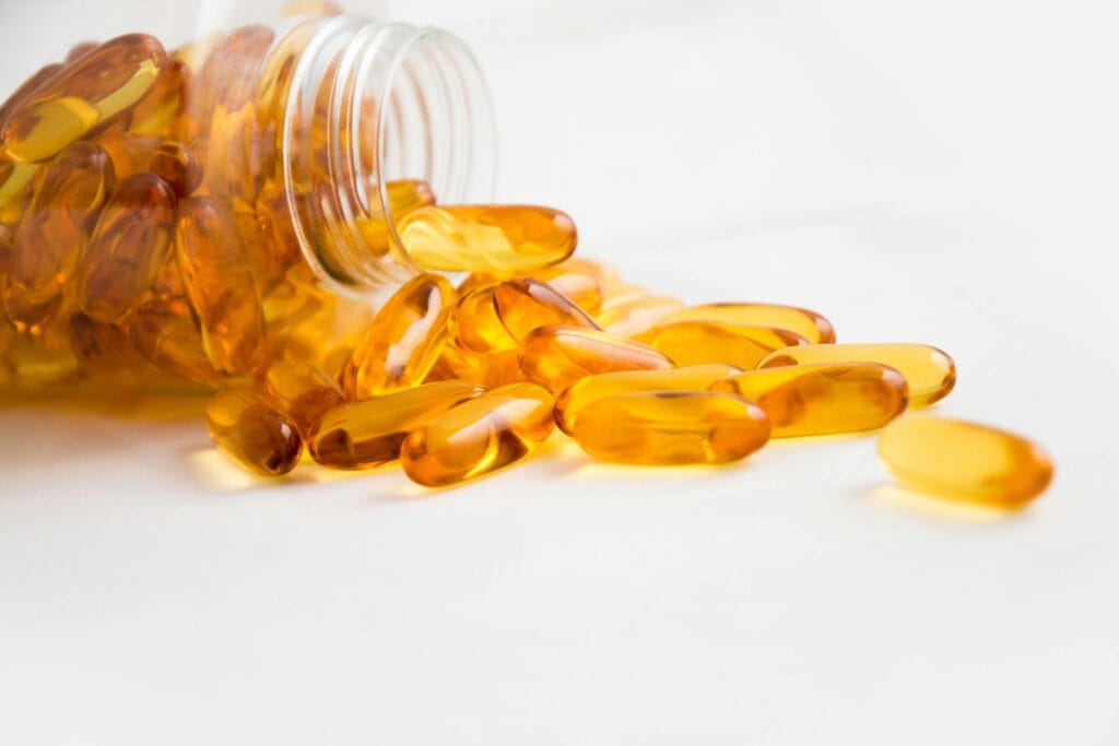 Spilled bottle of golden fish oil capsules on a light surface.